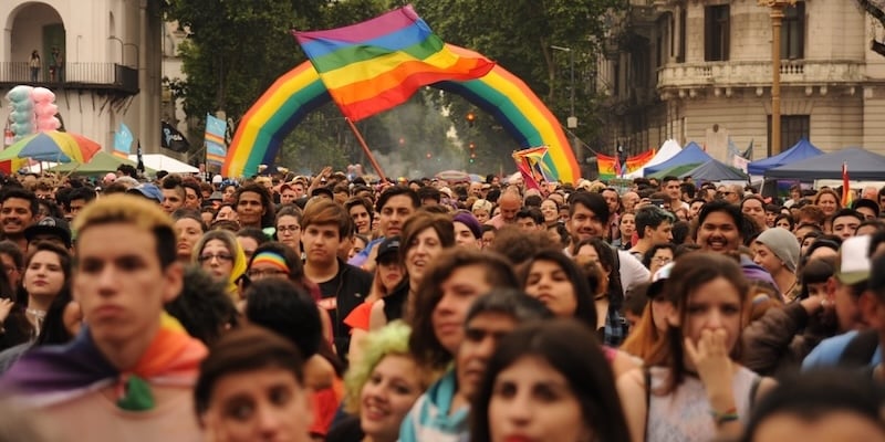 A large inflatable balloon in the shapes and colours of the rainbow is placed behind a large group of people walking during a Pride march in Argentina